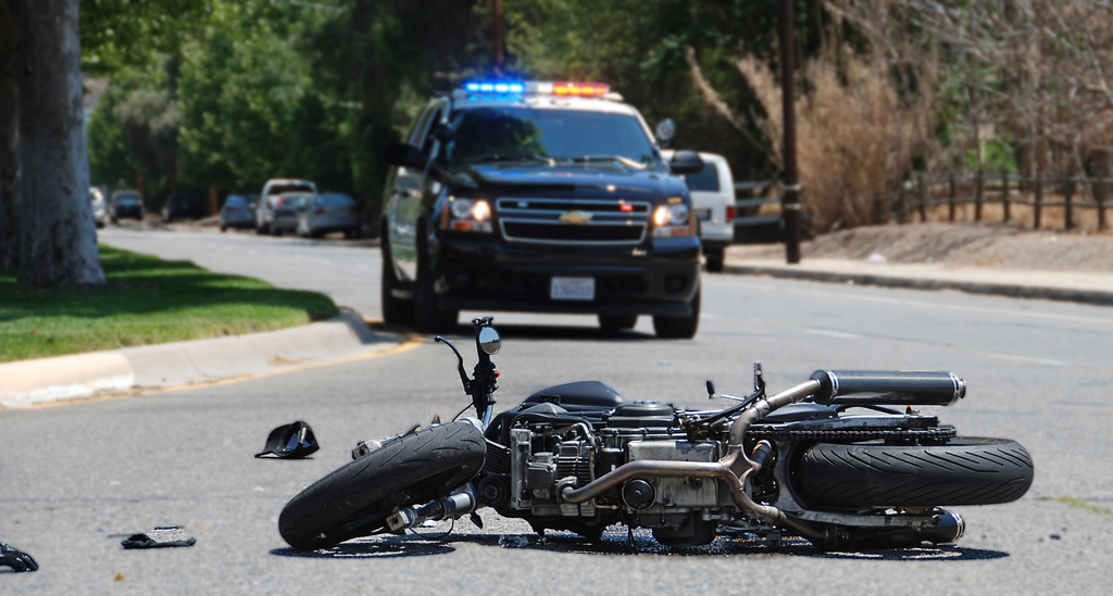 damaged motorcycle lies on the street, police car arrives in the background