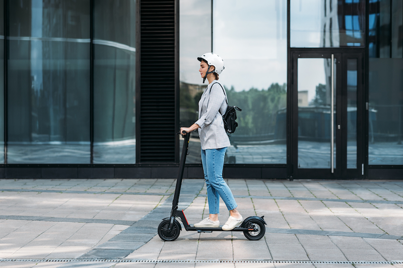 Side view of a young businesswoman riding electric scooter with a helmet on