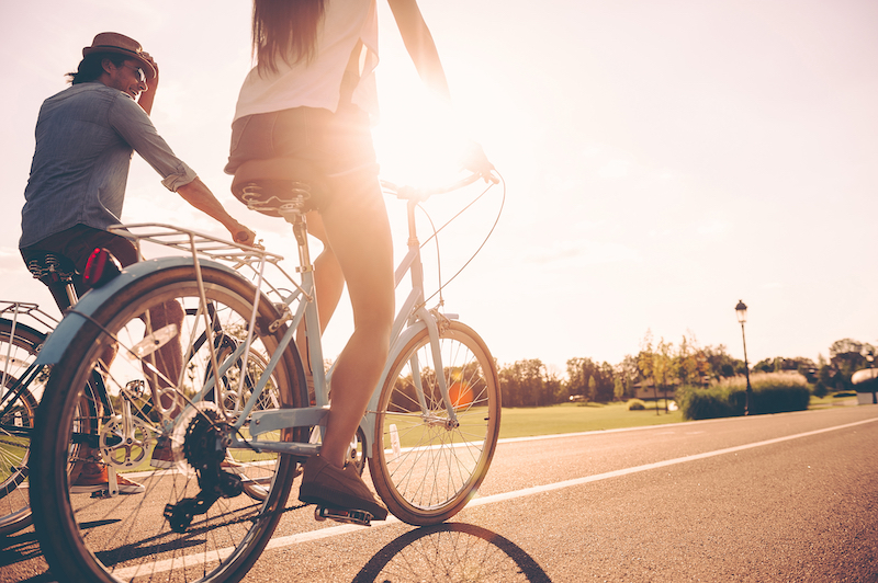 Cycling together. Low angle view of young people riding bicycles along a road together