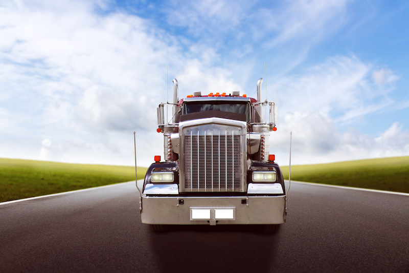 Truck driving on country road against blue sky