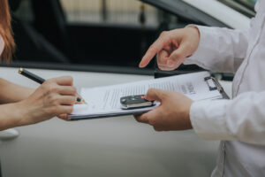 A contract being signed. We can see the hands of both people, with one holding the contract and telling the other where to sign