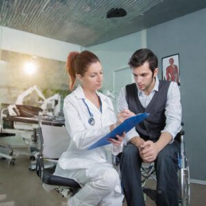 A man in a wheelchair in a hospital with a female doctor sitting next to him while going over documentation