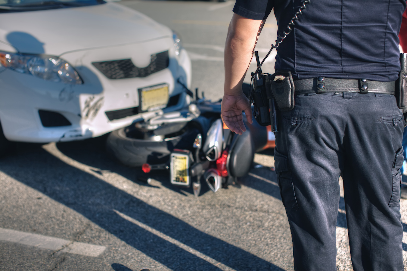 The aftermath of a car having crashed into a motorcycle, with a police officer (back turned to camera) looking at the damage